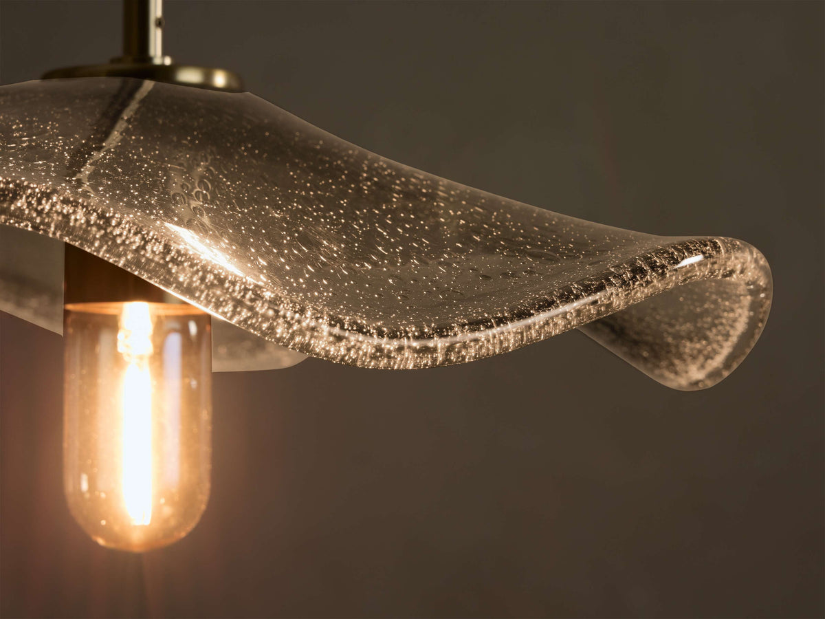 Close-up of a wavy, clear bubbled glass light shade with a warm glowing Edison bulb and a brass fixture.