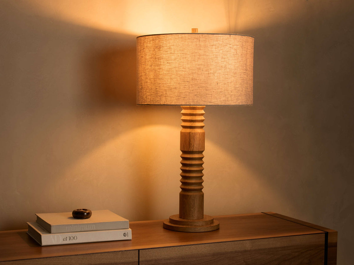 Front view of an illuminated natural wood Fluted Table Lamp with a light beige fabric cylindrical shade.