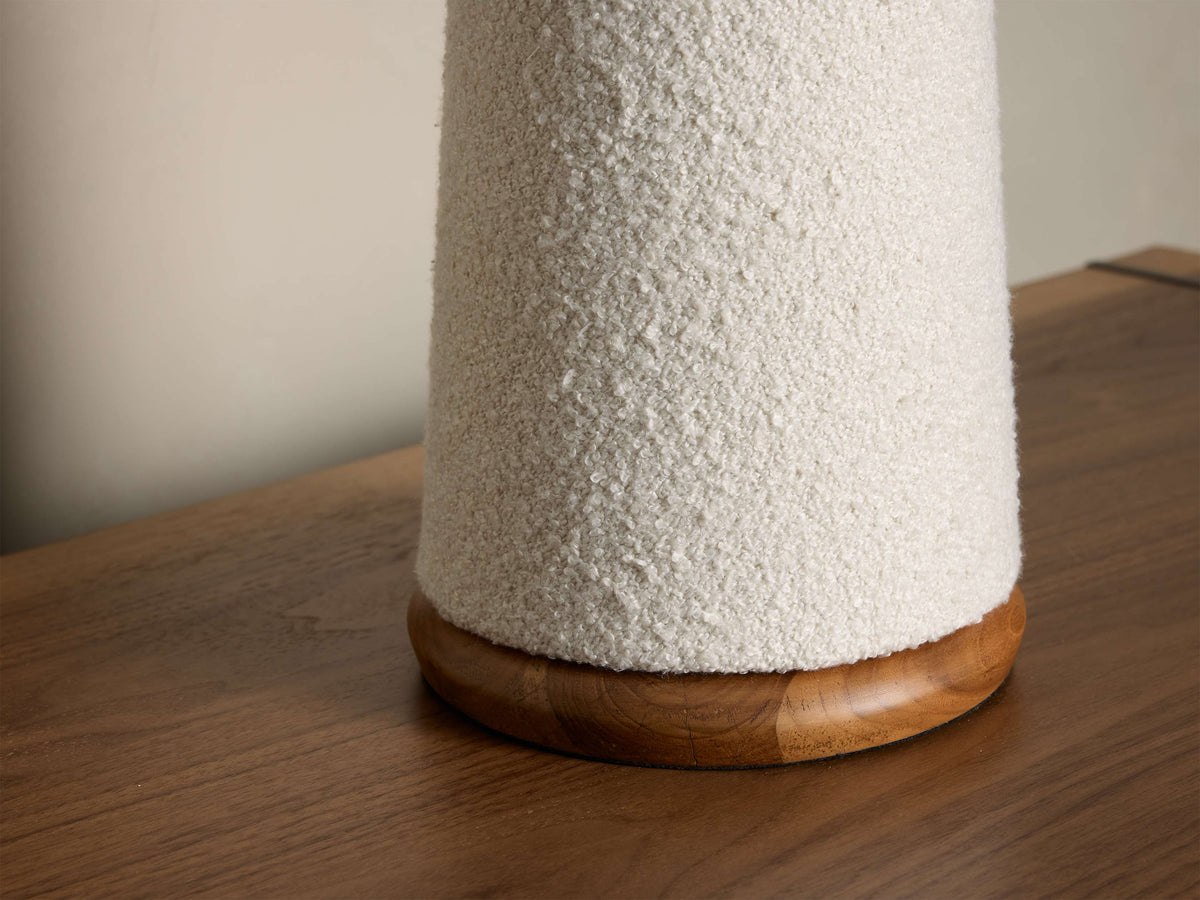 Close-up of a white bouclv©-textured base of a decorative object with a round wooden bottom on a wood table.