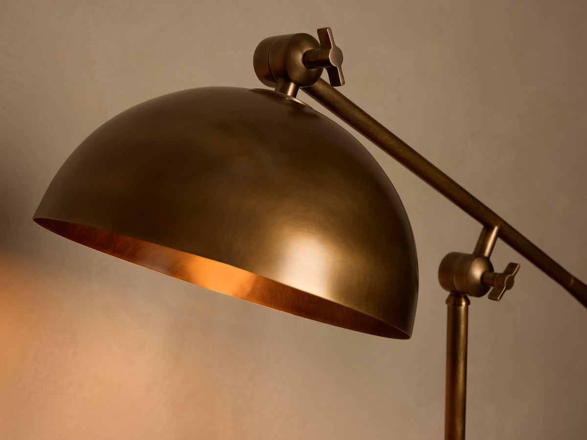 Close-up of antique brass dome lamp shade with warm, reflective interior. Features adjustable arm with knurled knobs.