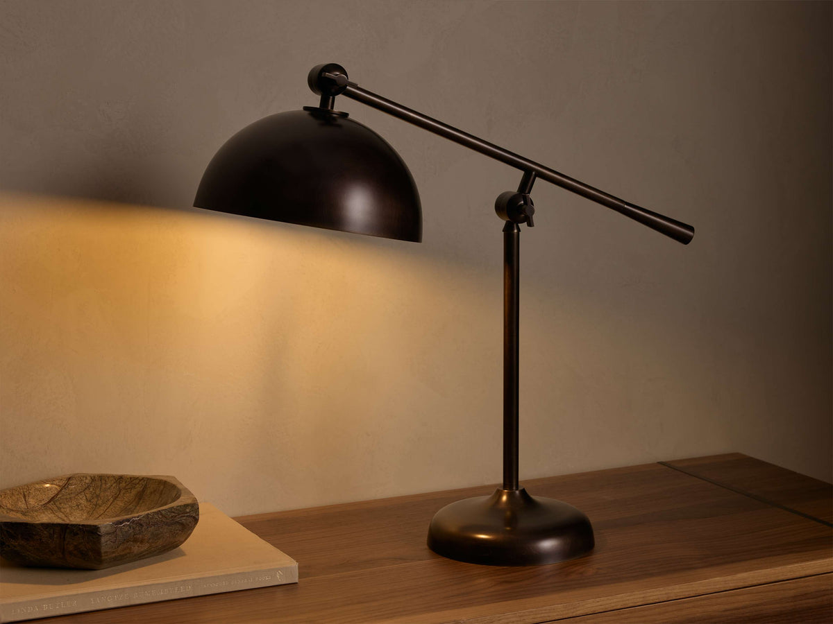 Front view of the oxidized antique brass Sigmund Task Table Lamp, with its adjustable arm and dome shade casting warm light.