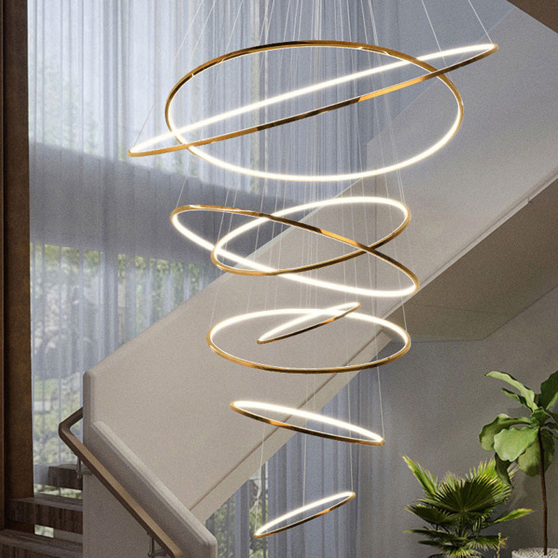 Eight-ring gold chandelier flowing through a bright stairwell, balancing substantial light output with a delicate suspended appearance.