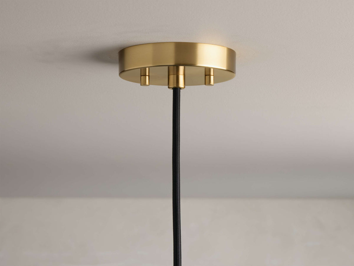 Close-up of circular gold ceiling canopy with three fasteners and a hanging black braided cord.