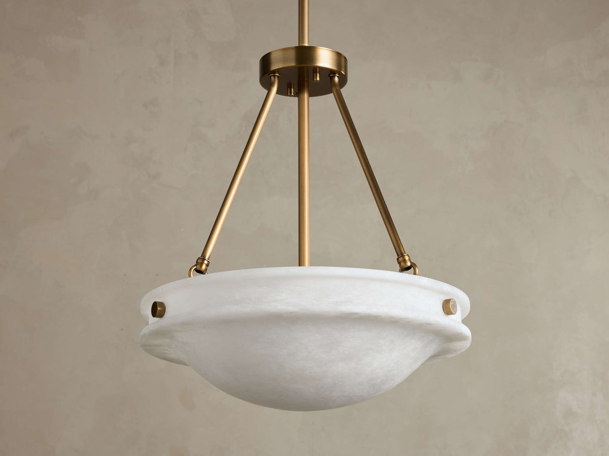 Front view of the Edith Pendant, featuring a white, subtly variegated alabaster stone bowl shade and a brass finish frame.
