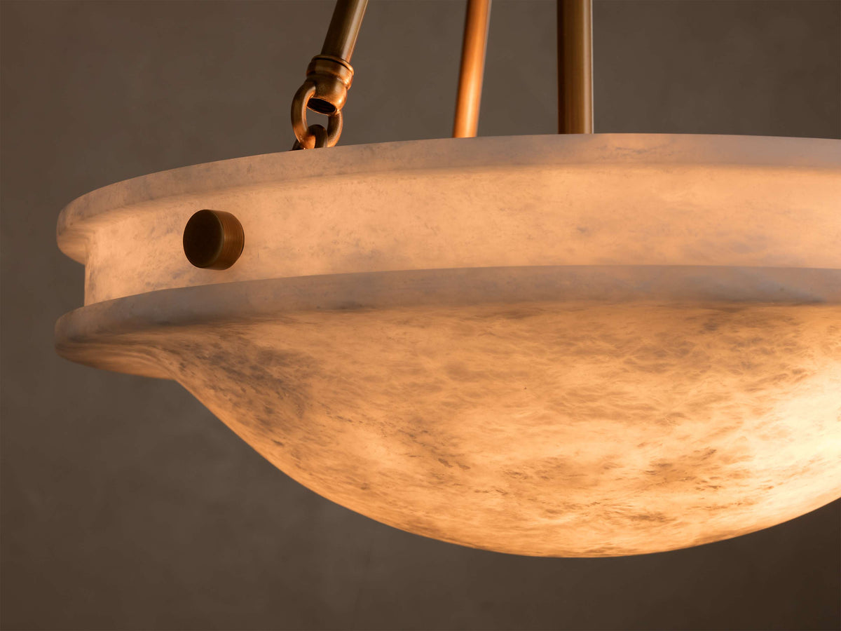 Close-up of the alabaster Edith Pendant's shade, glowing warmly, revealing natural marbling and a round brass button detail.