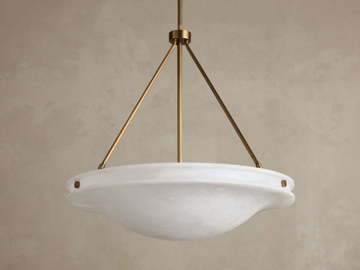 Front view of the Edith Pendant, a round white alabaster stone shade with subtle marbling, supported by three brass-finished rods.