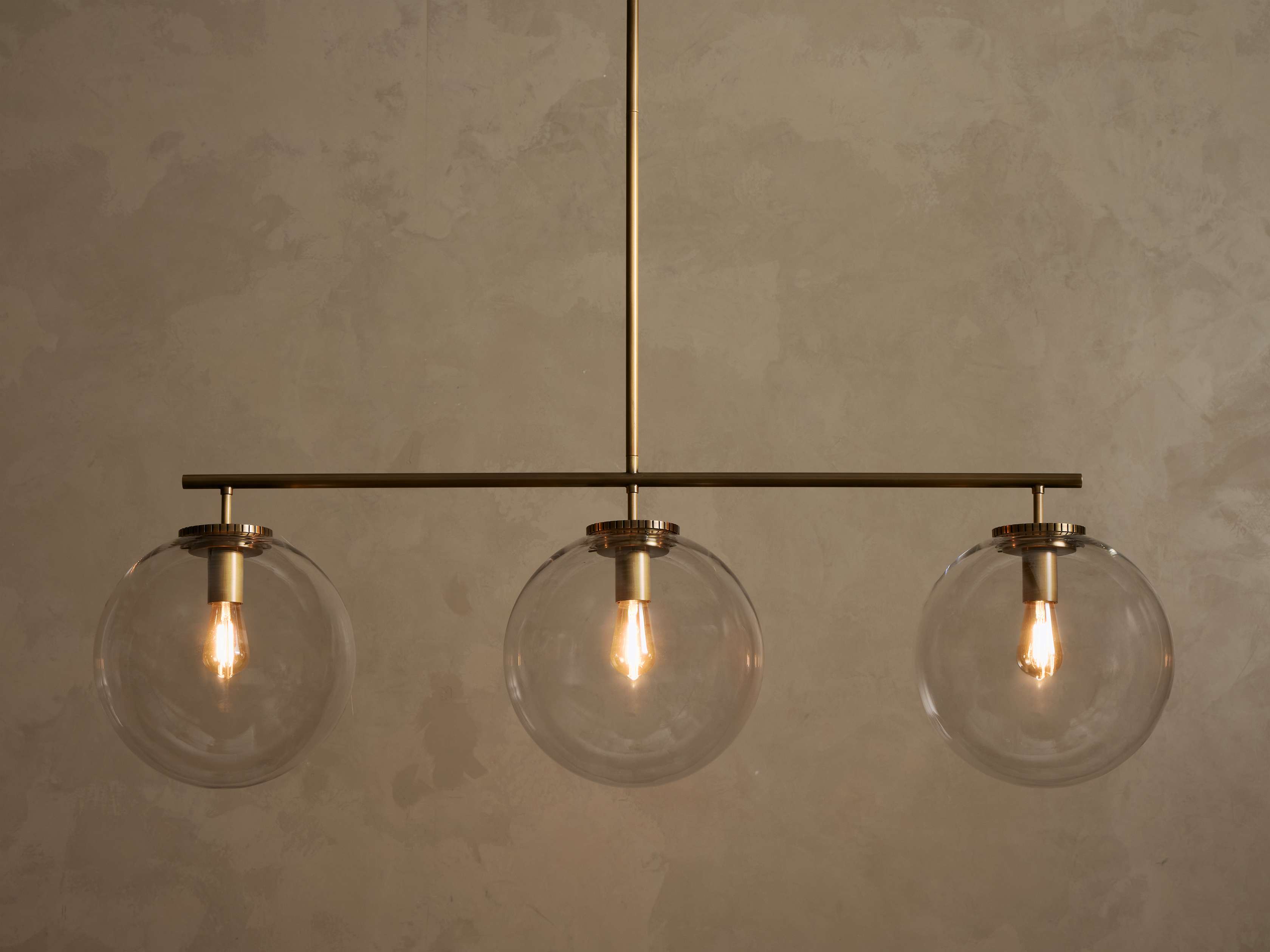 Front view of a brass chandelier with three clear glass globe shades, each containing an illuminated filament bulb.