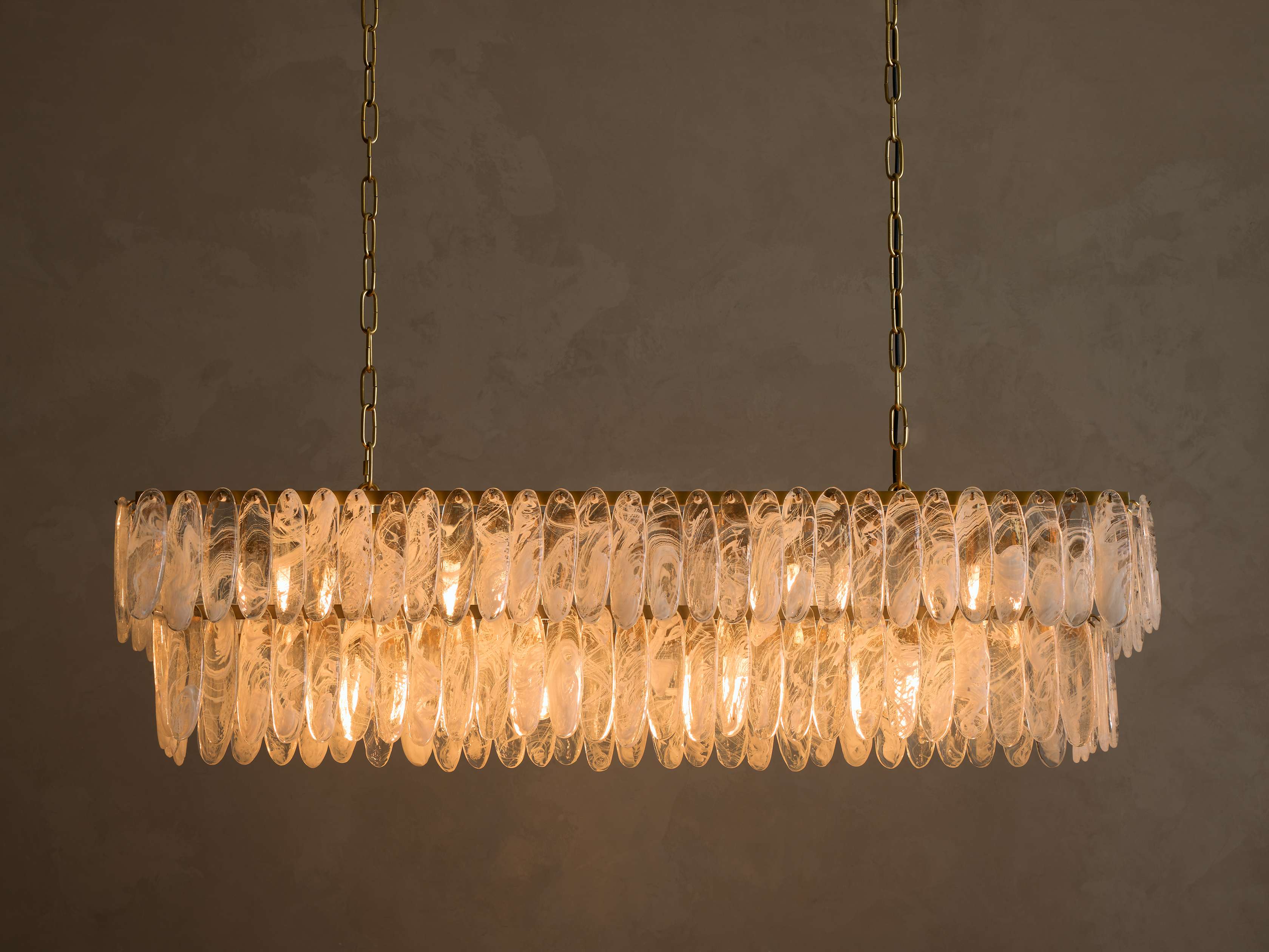 Gold rectangular chandelier, two tiers of illuminated clear oval glass with frosted swirls, suspended by chains.