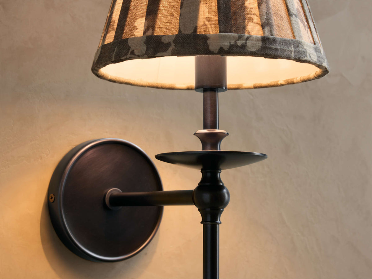 Close-up of the antique bronze Winslow Single Sconce, featuring an illuminated fabric shade with muted striped and floral patterns.