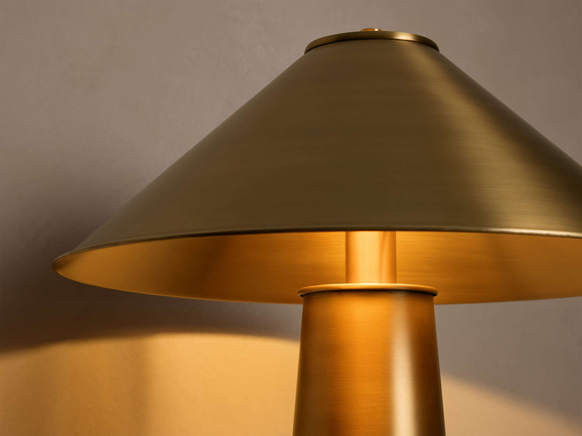 Close-up of the antiqued brass Ombra Metal Table Lamp, with its conical shade glowing warmly from within.