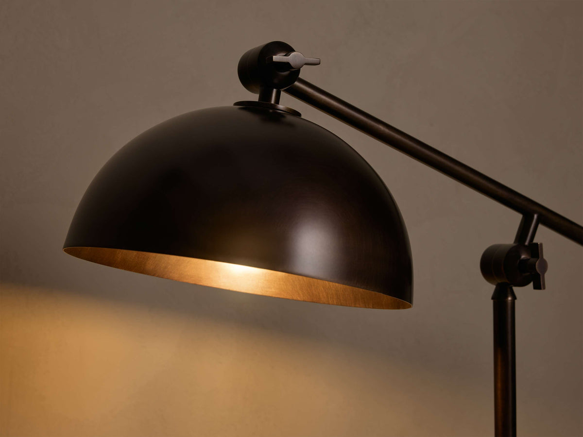 Close-up of the Sigmund Task Table Lamp with its oxidized antique brass finish dome shade angled down, revealing a warm gold interior and glowing light.