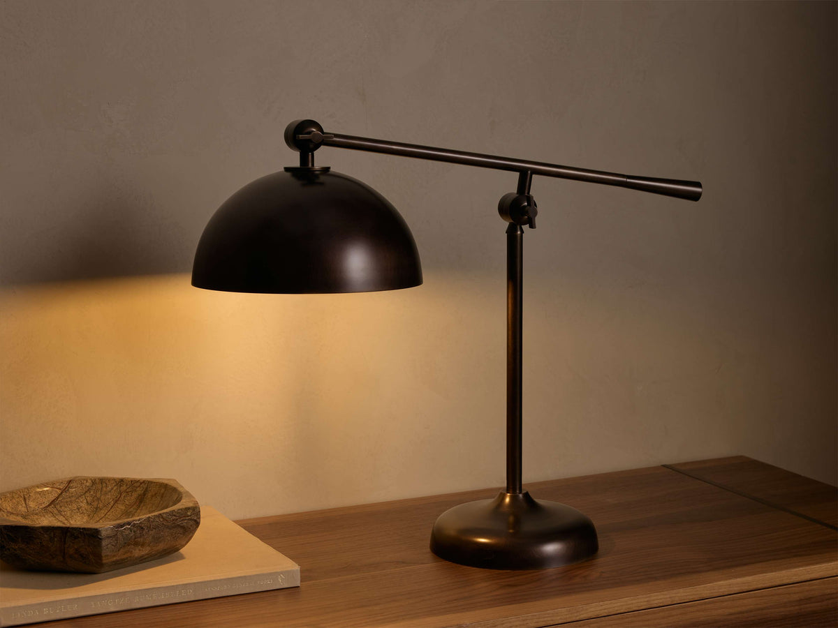 Front view of the oxidized antique brass Sigmund Task Table Lamp with pivoting arm and adjustable dome shade, illuminating a wooden surface.