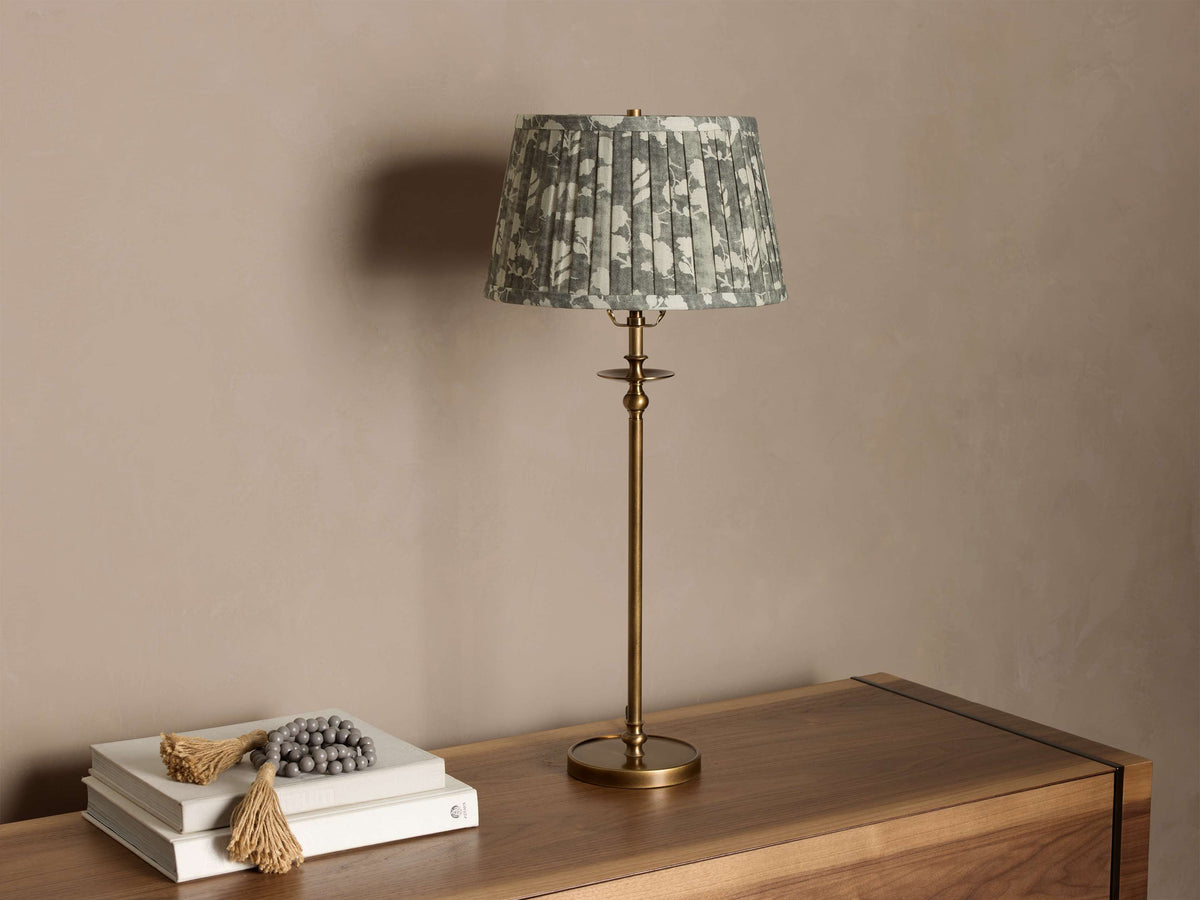 Winslow Table Lamp with an antique brass base and a pleated greenish-gray floral fabric shade on a wooden surface.