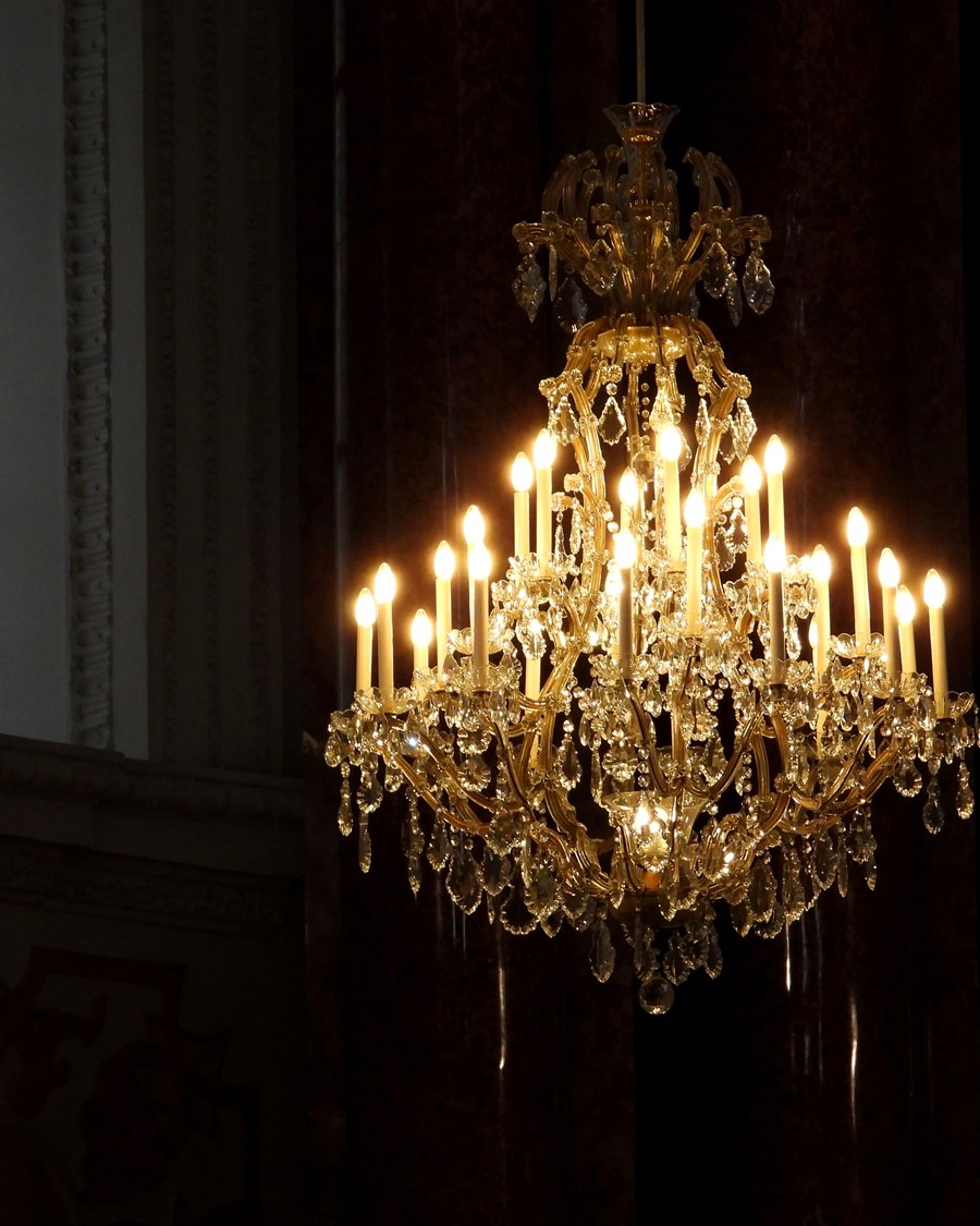 Tiered crystal chandelier with multiple candle arms against a dark ground