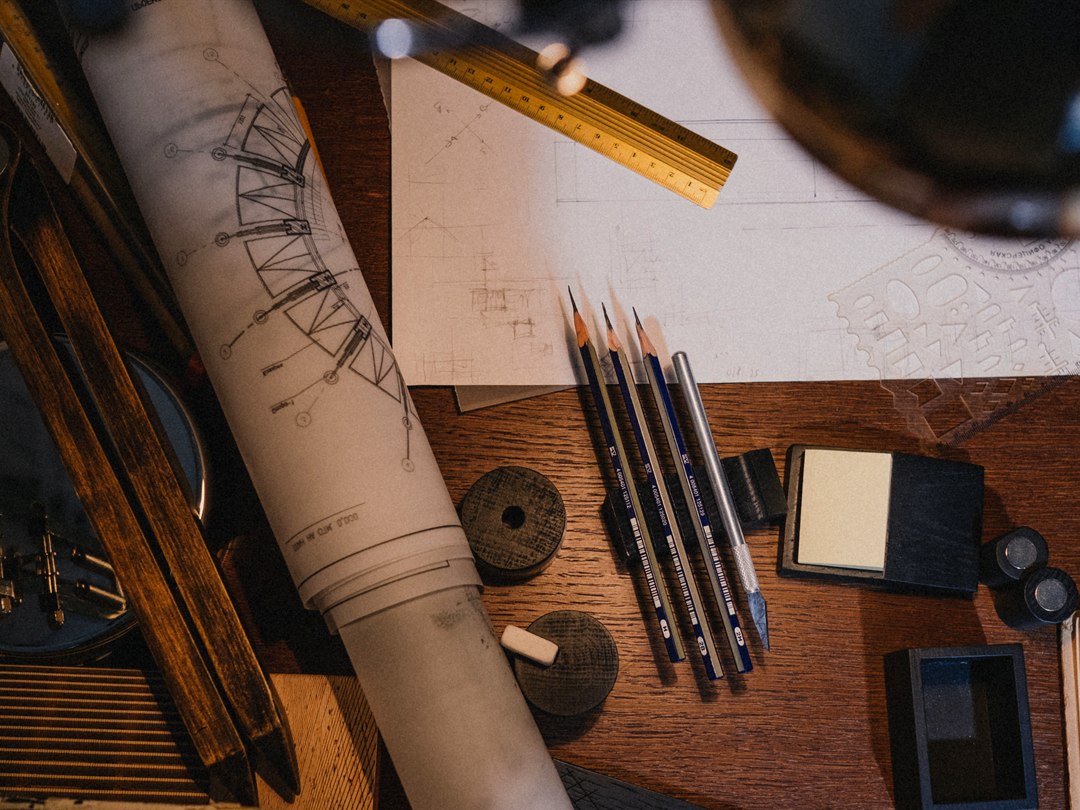 Rolled technical drawing with drafting compass and pencils on a timber desk
