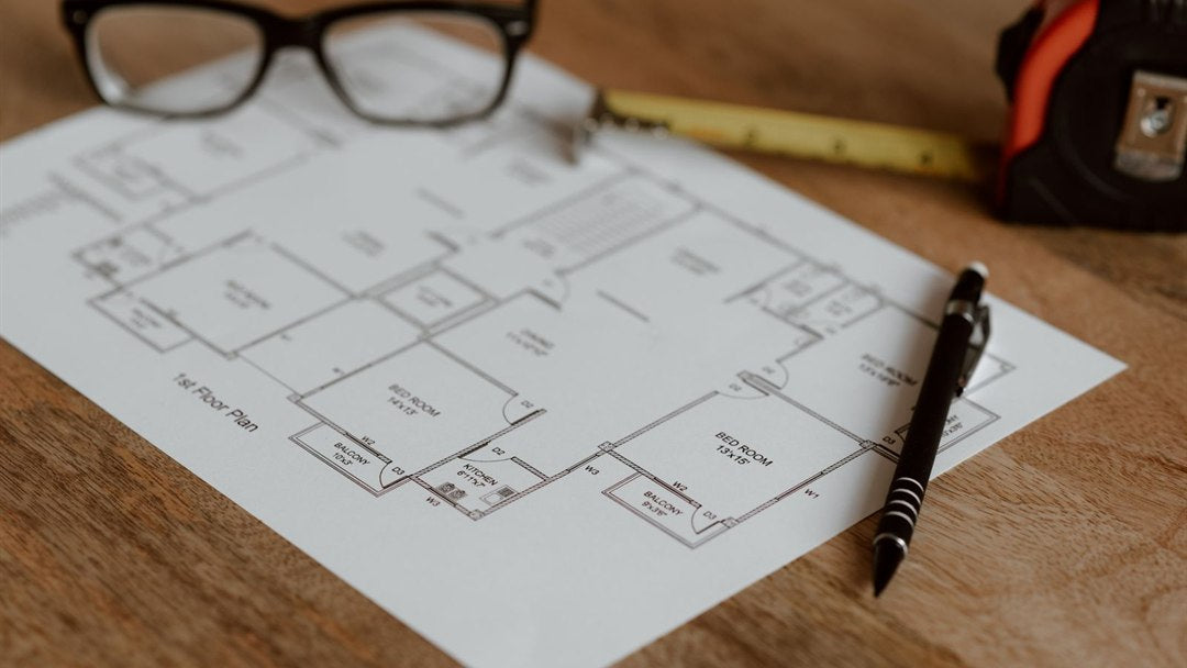 Floor plan drawing with pen, glasses and a tape measure on a wood desk