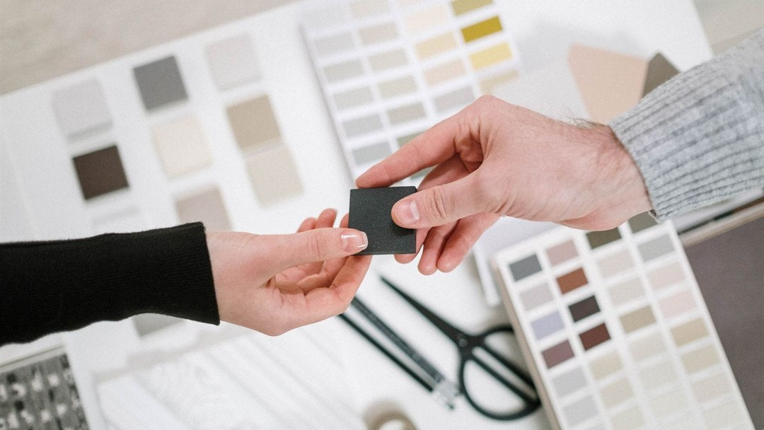Designer handing over a material sample above a spread of neutral swatch cards